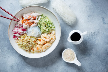 Above view of cold korean kuksi soup with chicken meat and chicken bouillon, horizontal shot on a light-blue stone background