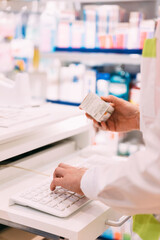 Close up of pharmacist hand holding medicine and using computer in pharmacy store