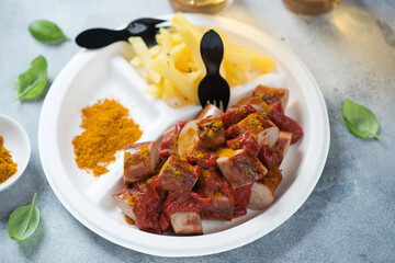 White takeaway plate with currywurst or german traditional sausages served with tomato sauce, curry and fries, studio shot on a light-blue stone background