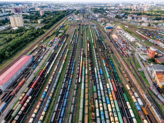 Aerial top view on railways with various colorful cargo wagons. Transportation of various goods by rail. Import and export logistics. Industrial landscape, city on background. Freight sorting station.