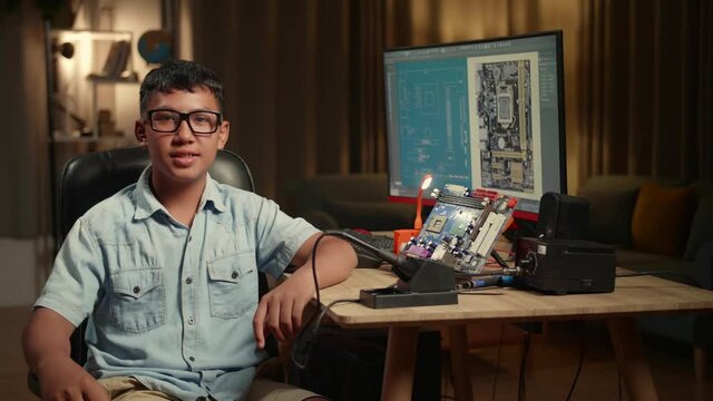 It Asian Boy Is Working With Desktop Computer And Mainboard In Home, Display Showing Cad Software. He Turns And Warmly Smiles Into The Camera, Genius Children Concept
