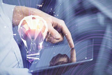 Double exposure of man's hands holding and using a digital device and bulb hologram drawing. Idea concept.