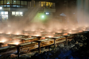 Close up view of yubatake hot spring mist and steam covered wooden track at night in Kusatsu town in winter ,Gunma Japan.