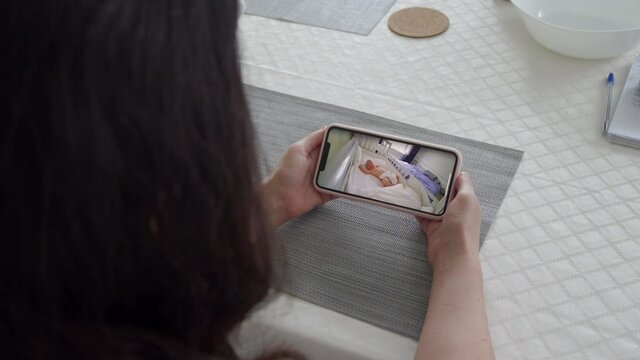 Mother using ip wireless security camera as baby video monitor on mobile phone, woman watching her sleeping baby in real-time. High quality 4k footage