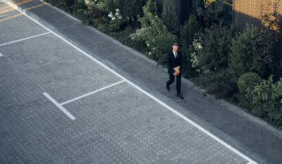 Top view of mature man in full suit carrying laptop while walking outdoors