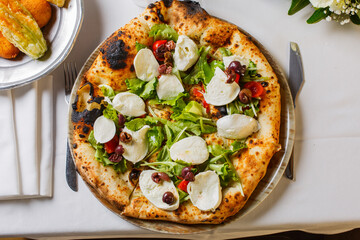 Pizza napoletana con mozzarella di bufala fresca, pomodori, rucola, basilico e olive