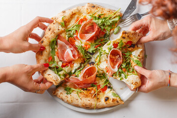 Mani mentre prendono due fette di pizza napoletana con rucola, prosciutto crudo, pomodori e mozzarella di bufala