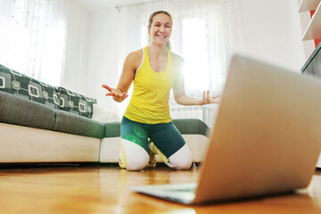 Smiling fitness instructor kneeling on the floor at home and having online class with students.