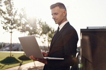 Confident mature businessman working on laptop while standing outdoors