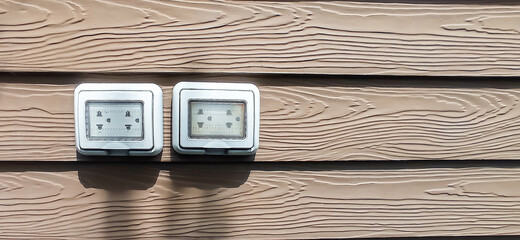 Waterproof electrical sockets installed outdoors on dark wooden walls.