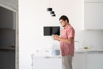 Young man holding a disposable plastic bag with food delivery at the modern kitchen