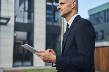 Confident mature businessman using digital tablet while standing outdoors near office building