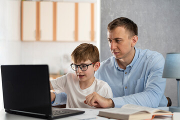 Dad teaches his son to work with computer program. Dad helps his son do homework. Online learning, distance learning