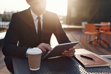 Concentrated mature businessman using digital tablet while sitting in cafe outdoors
