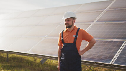 Close up portrait of male electrical worker in protective helmet standing near solar panel. Clean energy production. Green energy. Solar farm. Cheerful man smiling while standing at solar power farm