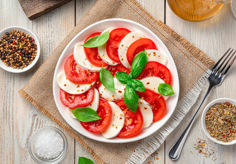A plate of caprese salad with tomatoes, mozzarella and basil on a light wooden background.
