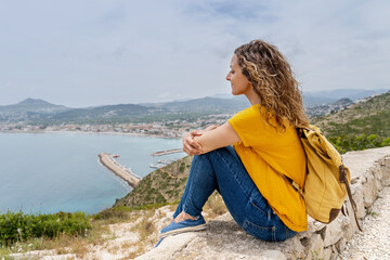 Horizontal view of woman sit on top of a mountain. Summer lifestyle and adventure with backpack.