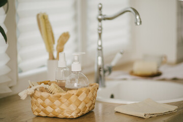 Kitchen interior with natural eco-friendly zero waste cleaning items: brushes, rugs, soap, spray and sponges in a wicker basket.