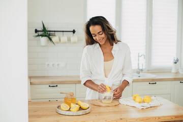 Young woman making lemonade in a kitchen of cozy house. Homemade healthy drink.