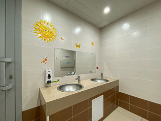 Public toilet for children. A washbasin, drawings on the walls. Mirrows