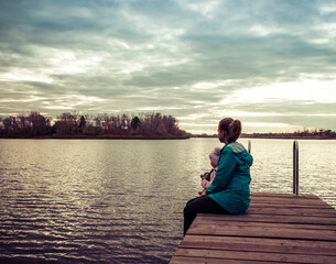 mom and daughter are sitting on the pier at sunset