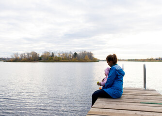 mom and daughter are sitting on the pier at sunset