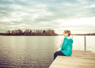 mom and daughter are sitting on the pier at sunset