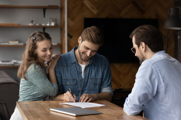 Happy millennial couple signing property purchase contract, insurance agreement, filling bank...