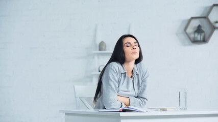 worried woman with closed eyes breathing while sitting at desk in office - obrazy, fototapety, plakaty