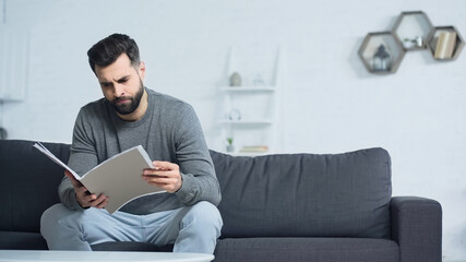 dissatisfied man looking at folder while sitting on sofa in living room