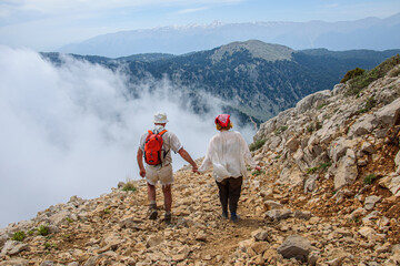 The guy helps to go down the girl who is afraid from the slope of Tahtali Dag. Turkey. Lycian trail - obrazy, fototapety, plakaty