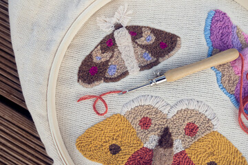Closeup of embroidered butterflies on two-thread cloth in a hoop with punch needle and brick-red...