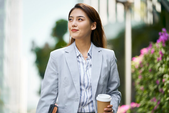 Successful Asian Business Woman Walking On City Street Holding Cup Of Coffee