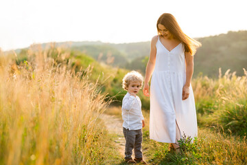 Beautiful woman in a dress walks in nature with her son with curly hair