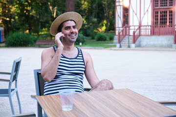 Tourist talking on the phone resting, smiling, sitting on a bar summer terrace.