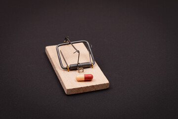 Pharmaceutical Addiction or Big Pharma Trap - Colored Pill or Capsule in Wooden Mousetrap on Black...