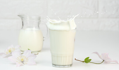 full glass cup of fresh milk with splashes stands on a white table, healthy breakfast