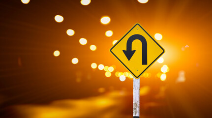 Left u-turn sign on pole, streetlights bokeh background. Concept for traffic sign at night.