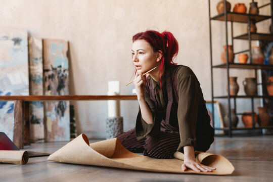 Young woman artist sitting on a floor of an art studio
