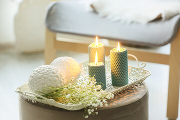 Tray with burning candles and flowers on pouf in room