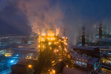 Night top view of steel plant at night with smokestacks and fire blazing out of the pipe. Industrial panoramic landmark with blast furnance of metallurgical production