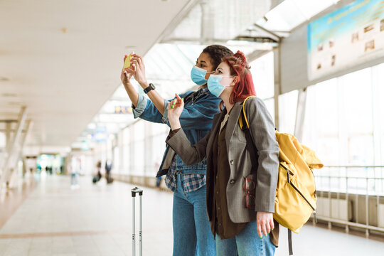 Multiracial women in face masks taking photo on cellphone at train station