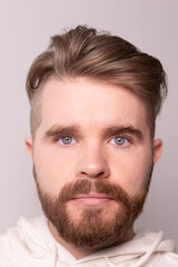 Obraz premium Portrait of young male with beard and mustache and trendy hairdo. Wears casual hoodie, has serious expression in studio against white background