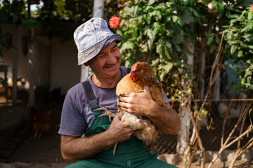 Portrait of happy caucasian farmer holding a brown hen outdoor. Smiling mature man with chicken in hand with copy space. © diignat