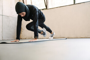 Young muslim woman in hijab doing exercise while working out indoors