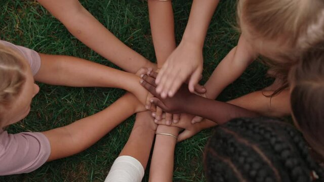 Mixed race children and teacher stacking hands in circle