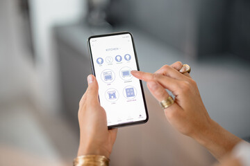 Smart phone with running mobile application to control smart devices in the kitchen. Female controlling smart devices with phone at home. Smart home concept