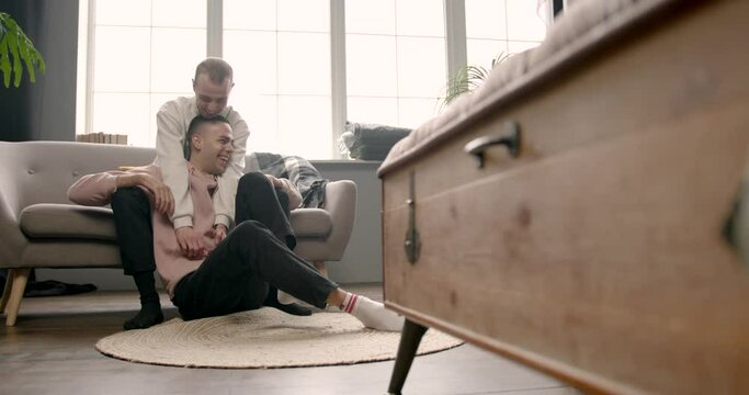 Delighted gay couple watching television together at home