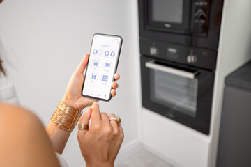 Smart phone with running mobile application to control smart devices in the kitchen. Female controlling microwave or oven with phone at home. Smart home concept