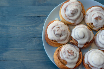 Homemade swirled rosy buns covered with white cream on a blue plate on the right on a blue wooden background top view